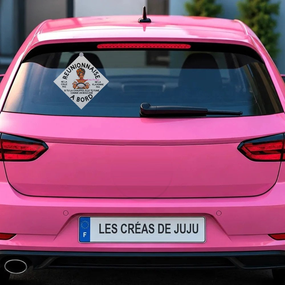 Plaque ventouse "Réunionnaise à bord" fond blanc, si tu la chauffes elle te fume comme un boucané, fixée derrière la lunette arrière d'une voiture rose - Les Créas de Juju