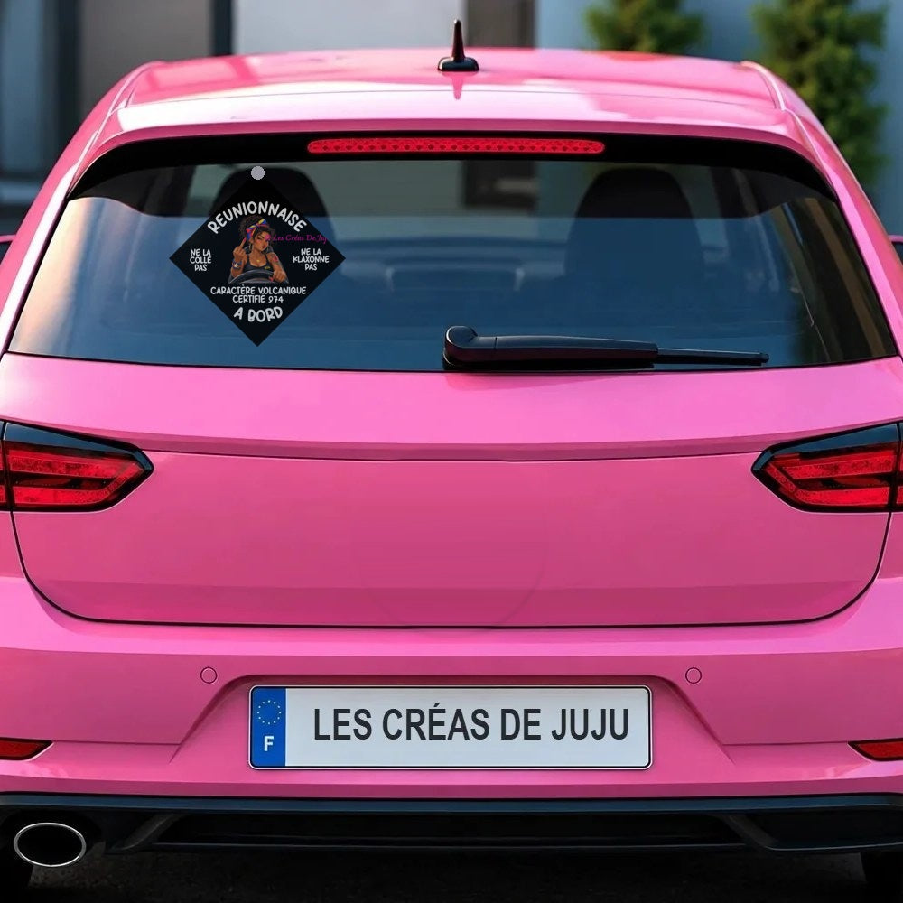 Plaque ventouse "Réunionnaise à bord" fond noir, caractère volcanique certifié 974, fixée derrière la lunette arrière d'une voiture rose - Les Créas de Juju